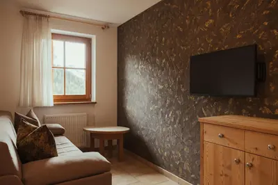 a living room with a couch and a tv on a wall at Refugium LaFlu Apartments in Corvara in Badia