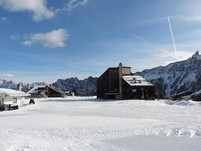 a building in the snow with mountains in the background at Casa Mowgli - Residence Sussy in Falcade