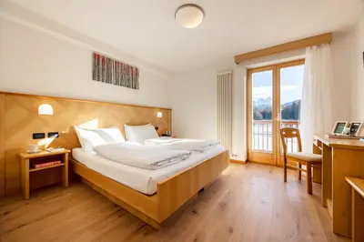 a bedroom with a bed and a desk and a window at Phi Hotel Bellamonte in Predazzo