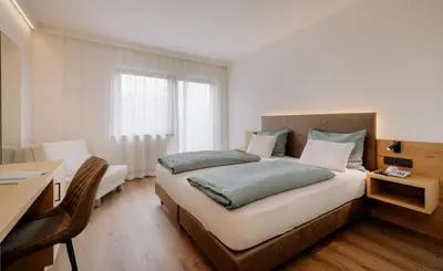 a bedroom with a large bed and a desk and a window at Garni-Hotel Farmerhof in Parcines