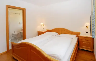 a bedroom with a large wooden bed with white sheets at Urthalerhof in Castelrotto