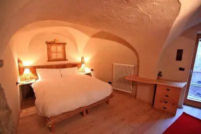 a bedroom with a bed and a table and a window at Maso Toneto in Castello di Fiemme