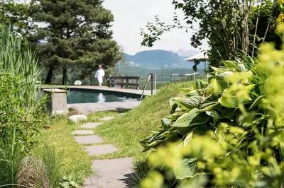 a garden path next to a swimming pool with a person in the background at Hotel Weingut Stroblhof in Appiano sulla Strada del Vino