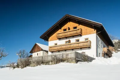 a house with a wooden roof in the snow at Huberhof Morgensonne in Terento