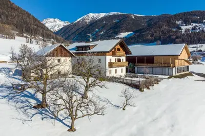 a house in the snow with mountains in the background at Huberhof Morgensonne in Terento