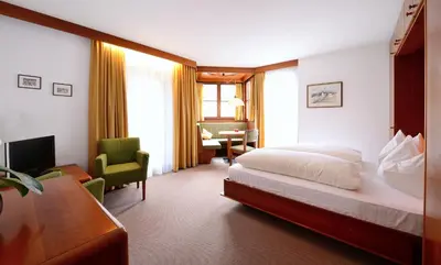 a hotel room with a bed and a chair and a desk at Residence Bacher in Valdaora