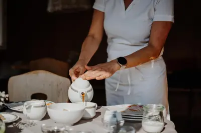 a woman pouring coffee into a tea pot on a table at Hotel Berghaus Rosengarten in Nova Levante