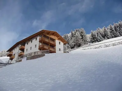 a building on a snow covered hill with trees at Putzerhof in Funes