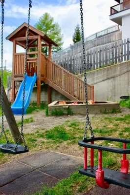 two swings in a park with a wooden playground at Gasthaus Oberkirn in Schenna