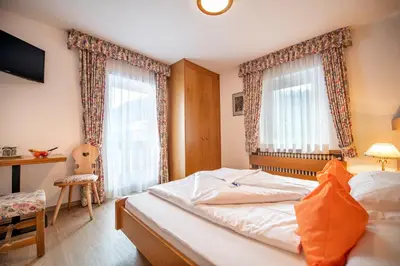 a small bedroom with a bed and two windows at Garni Bondi in Selva di Val Gardena