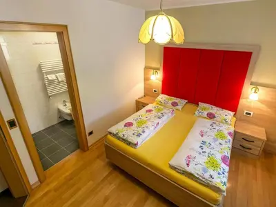 a bedroom with a bed with a red headboard and a bathroom at Amazing apartment house Diamant with breathtaking view in Santa Cristina in Val Gardena