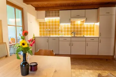 a kitchen with white cabinets and a vase of flowers on a table at Ganoihof apartments in Funes