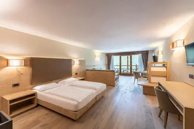 a bedroom with a large bed and a desk at Design & Suite Hotel Ciarnadoi in Vigo di Fassa