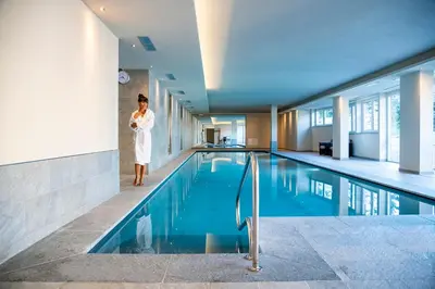 a woman standing next to a swimming pool at Design & Suite Hotel Ciarnadoi in Vigo di Fassa