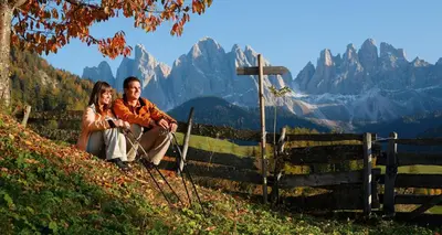 a man and woman sitting on a hill with mountains in the background at Apartments Dolomites 