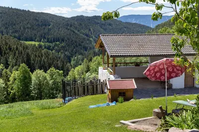a house with a red umbrella on a green hill at Spitalerhof Apartment & Sauna in Verano