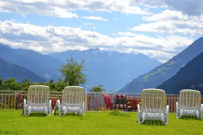 a group of chairs sitting on a deck with a view of mountains at Pension Apartments Klotznerhof in Schenna