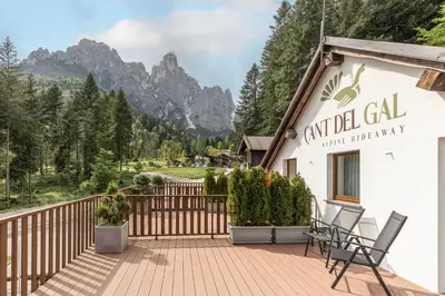 a building with chairs on a deck with mountains in the background at Hotel Cant del Gal in Fiera di Primiero