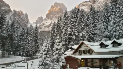 a house covered in snow in front of a mountain at Hotel Cant del Gal in Fiera di Primiero