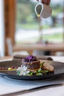 a person drizzling sauce on a plate of food at Hotel Cant del Gal in Fiera di Primiero
