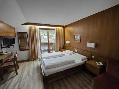 a bedroom with two beds and a desk and a window at Hotel Alpenblick in Sarntal