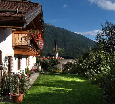 a house with a green yard with a church in the background at Haus Tirol in Molini di Tures