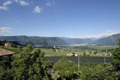 a white house on a hill with mountains in the background at Schloss-Hof in Appiano sulla Strada del Vino