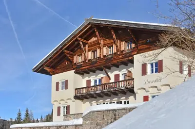 a building with a wooden balcony on top of snow at Hotel Bewaller in Obereggen
