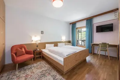 a bedroom with a bed and a chair and a tv at Hotel Bewaller in Obereggen