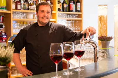 a man standing behind a bar with three glasses of wine at Almhotel Bergerhof in Sarntal