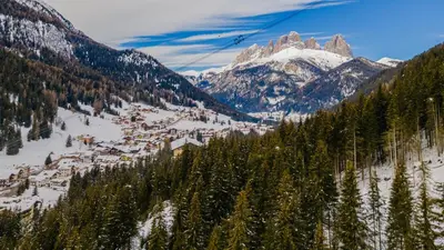 a snow covered mountain with a town and trees at Piccola Cesa Apartments in Canazei