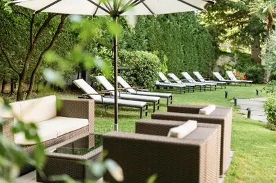 a row of chairs and an umbrella in the grass at Classic Hotel Meranerhof in Merano