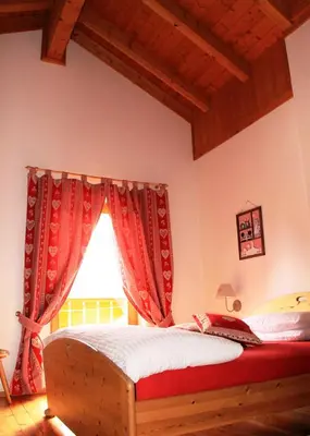 a bedroom with a bed with red curtains and a window at Garni Biancaneve Ruffrè-Mendola in Mendola
