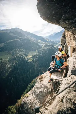 three people sitting on a bench at the top of a cliff at Wiesenhof Gardenresort in San Leonardo in Passiria