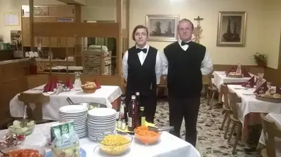 two men in tuxedos standing in front of tables at Pension Flora in Ora/Auer
