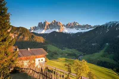 a house on a hill with mountains in the background at Wanderhotel Teiserhof in Funes