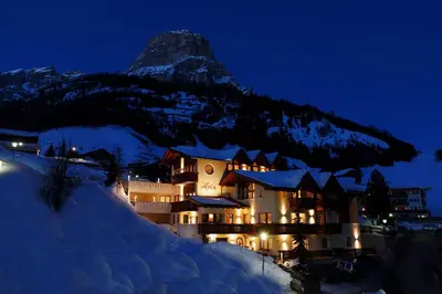 a hotel with a mountain in the background at night at Alpin Apartments Colfosco in Colfosco