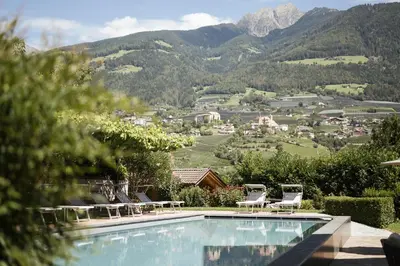 a swimming pool with chairs and mountains in the background at Hotel Eichenhof in Tirolo