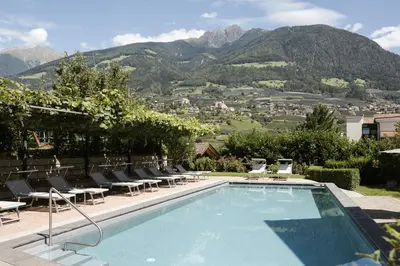 a swimming pool with chairs and mountains in the background at Hotel Eichenhof in Tirolo