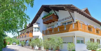 a white building with wooden balconies on a street at Hotel Villnerhof in Egna