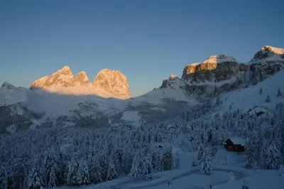 a snow covered mountain with a house in the foreground at Hotel Savoia in Canazei