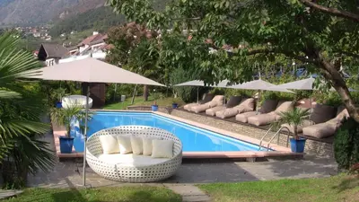 a swimming pool with chairs and umbrellas next to it at PALMENGARTEN Hotel Gstör in Lagundo