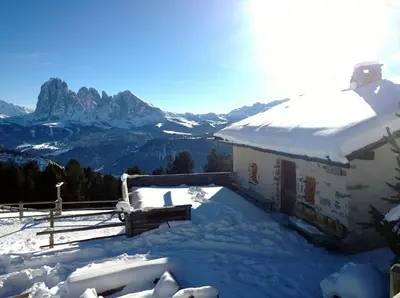 a house covered in snow with mountains in the background at Apartment Puciacia - Bauernhof in Santa Cristina in Val Gardena