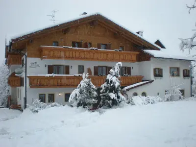 a house in the snow with trees in front of it at Hotel Thuinerwaldele in Vipiteno