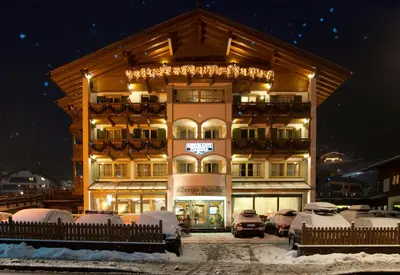 a building with snow covered cars parked in front of it at Hotel Pareda in Canazei
