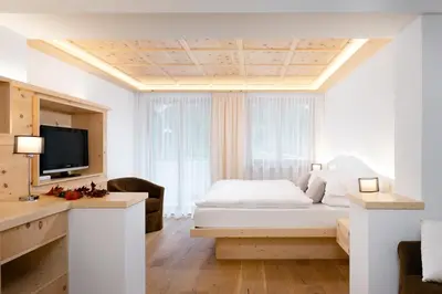 a white bedroom with a bed and a tv at Hotel Pareda in Canazei