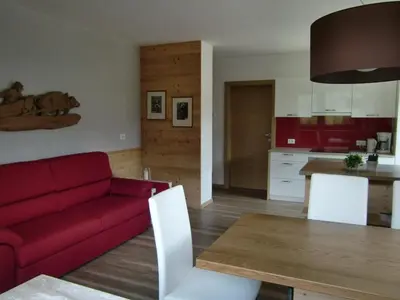 a living room with a red couch and a kitchen at Prà de Metz Apartments in Santa Cristina in Val Gardena