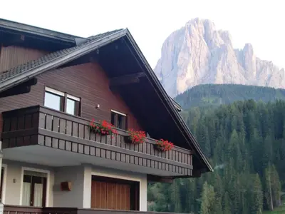 a house with red flowers on a balcony with a mountain at Prà de Metz Apartments in Santa Cristina in Val Gardena