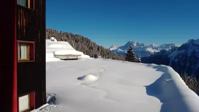 a snow covered hillside with a building and mountains at Piccolo Igloo in Falcade