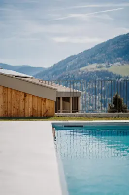 a swimming pool with a building and mountains in the background at Wanda Apartments in Parcines